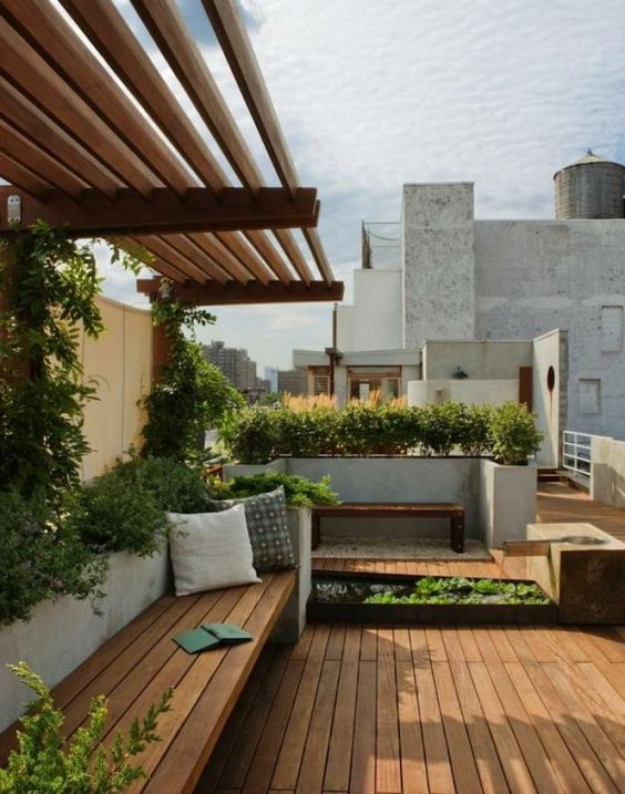 a modern terrace with a wooden deck, built-in furniture, a concrete lanter with greenery and other planters