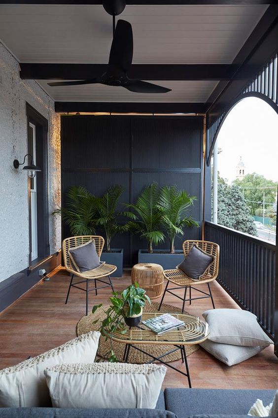 a modern terrace with black wooden slabs, wicker furniture, grey and neutral upholstery and potted greenery