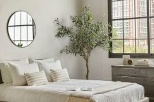a modern zen bedroom with a grey floating bed, a reclaimed wooden dresser, a statement plant, neutral bedding and a round mirror