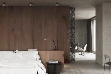 a modern zen bedroom with a wooden accent wall, an upholstered bed with white bedding, a black metal nightstand and lights