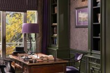 a moody vintage home office with grene cabinetry, mauve floral wallpaper, a stained desk and vintage chairs, purple accessories