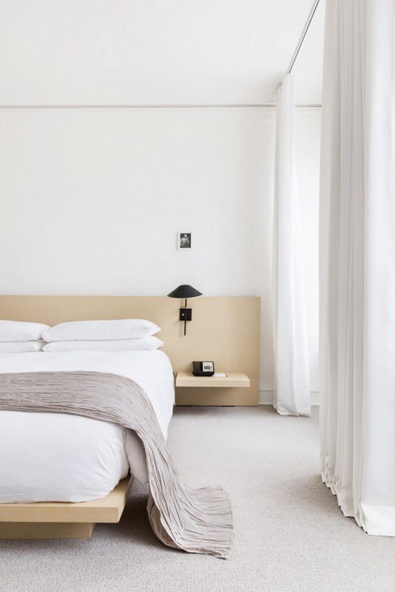 A neutral and welcoming zen bedroom with light colored wooden bed and nightstands, black sconces and white textiles