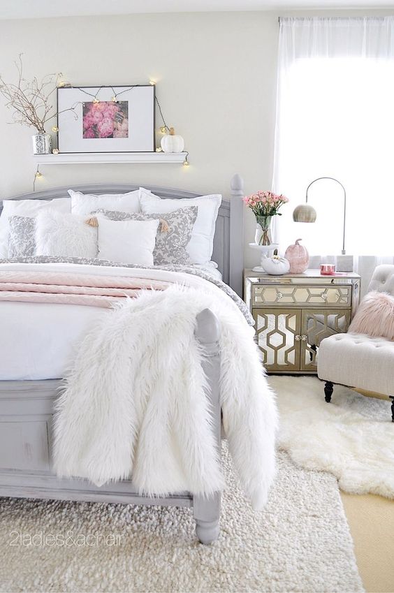 a neutral glam bedroom with a grey bed, mirror nightstands, faux fur rugs, blooms and lights over the bed