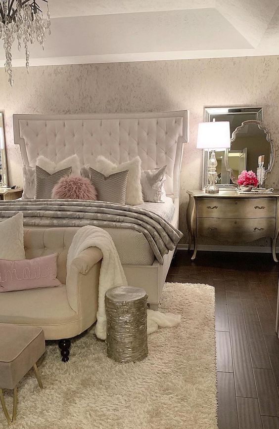 a refined glam bedroom in neutrals, silver furniture, a white upholstered bed, touches of pink and a crystal chandelier