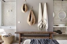 a relaxed zen bedroom united with a bathroom, with stone and concrete walls, a wooden bench, neutral bedding and baskets for storage