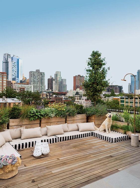 a simple and modern rooftop terrace with a wooden deck, mattresses instead of sofas and potted greenery