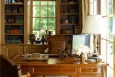 a vintage home office with built-in bookcases, a dark-stained vintage desk, matching leather chairs, a table lamp and some blooms