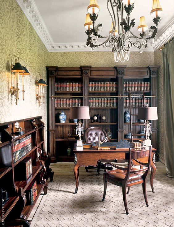 A vintage home office with dark stained bookcases and bookshelves, a dark stained desk and leather chairs, table and wall lamps and a cool chandelier