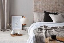 a zen-like bedroom in neutrals, with a woven headboard, neutral bedding, a low wooen table and some trays plus a floor lamp