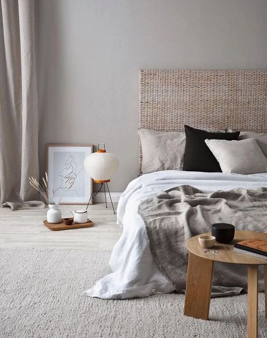 A zen like bedroom in neutrals, with a woven headboard, neutral bedding, a low wooen table and some trays plus a floor lamp