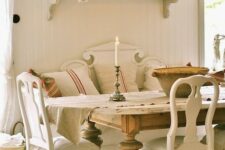 a French country chic dining room with neutral vintage furniture, a large stained vintage table, a wall-mounted shelf and a simple chandelier