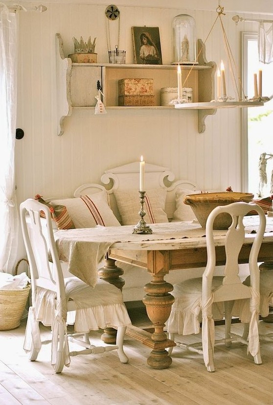 A French country chic dining room with neutral vintage furniture, a large stained vintage table, a wall mounted shelf and a simple chandelier