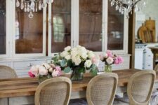 a French country dining room with several white buffets, a stained rustic table, vintage cane chairs and crystal chandeliers