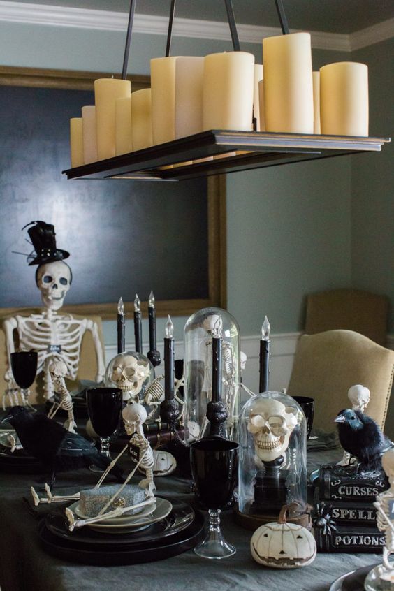 a Halloween table setting with black plates, goblets and candles, skulls and skeletons, white pumpkins