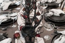 a Halloween tablescape with a white runner, dried roses, black branches, grye candles and elegant black plates