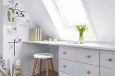 a Nordic attic home office in white, with a skylight, a built-in desk, a stool and a small gallery wall plus blooms