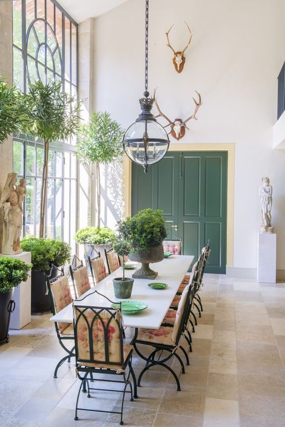 a Provence dining room with a large table, metal chairs with floral cushions, pendant lamps and potted greenery