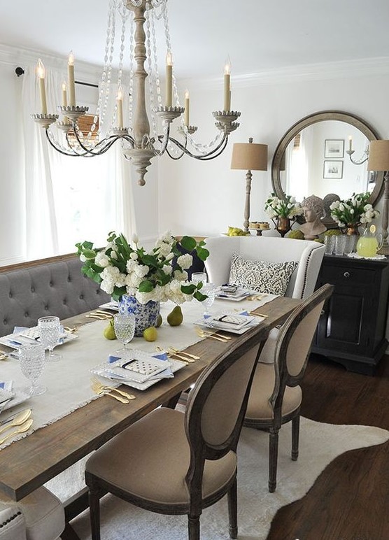 A beautiful French cream colored dining room with off white and beige furniture with a vintage loveseat, chairs, a beautiful chandelier and a round mirror