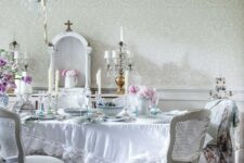 a beautiful shabby chic dining room with a crystal chandelier, white furniture, a ruffle tablecloth and blooms