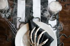a black and white Halloween table with a striped table runner, black napkins, skeleton hands, gold candleholders and snakes