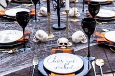 a bold and chic Halloween tablescape with black and white cheesecloth, black plates, goblets, plaid napkins and colorful candles and black branches