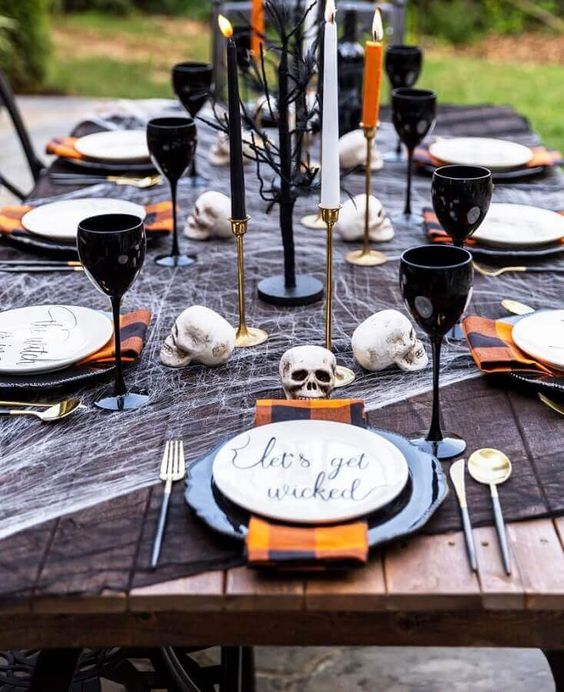 a bold and chic Halloween tablescape with black and white cheesecloth, black plates, goblets, plaid napkins and colorful candles and black branches