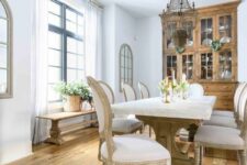 a breathtaking French chic dining room with a stained buffet, a vintage table with a stone tabletop, neutral chairs, a bench