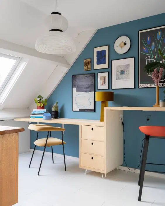 a bright attic home office with a blue accent wall, a desk with two different desktops, upholstered chairs and stools and a chic gallery wall