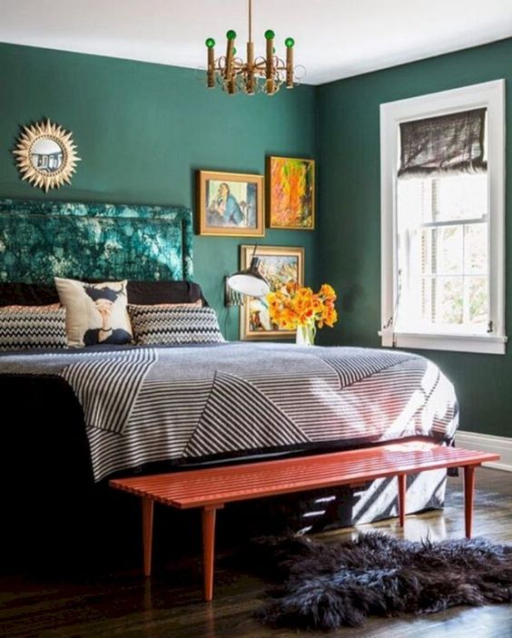 a bright fall bedroom done in emerald, with bright artworks, a red bench and metallics