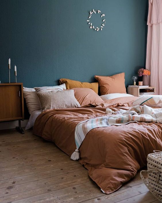 a bright fall bedroom with a dark green wall, rust and orange bedding and touches of stained wood