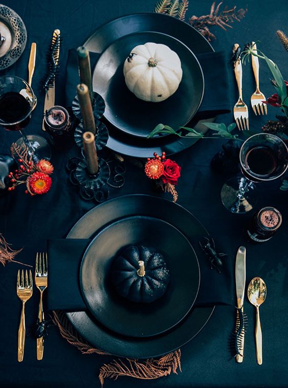 a bright modern Halloween tablescape with red blooms, spiders and snakes, gold cutlery, white and black pumpkins