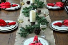 a bright winter tablescape with a burlap runner, red napkins, a pinecone and evergreen runner plus candles