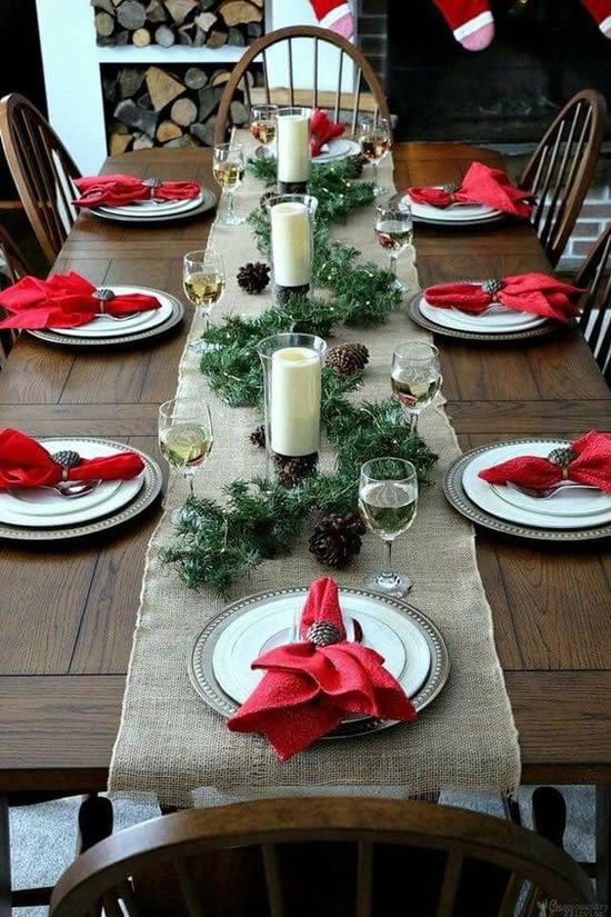a bright winter tablescape with a burlap runner, red napkins, a pinecone and evergreen runner plus candles