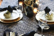 a chic Halloween tablescape with a spiderweb tablecloth, black napkins, black crows and pumpkins, candles and twigs plus a skeleton
