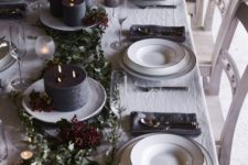 a chic dark tone winter tablescape with dark candles, greenery, berries, grey napkins and white porcelain