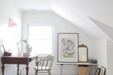 a clean and airy white attic home office with a planked floor, a vintage dark stained desk, a vintage chair, a bench, some artworks and a basket