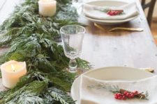 a cozy and homey winter table with an evergreen and pilalr candle runner, berries and evergreens plus gold cutlery