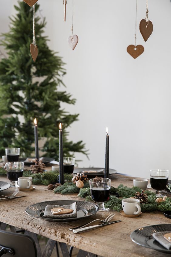 a cozy winter table with an evergreen, pinecone and nut runner, black candles and black plates plus gingerbread cookies over the table