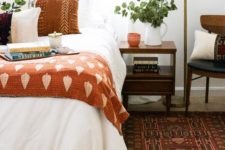 a fall colored bedroom with rust and orange textiles, a burgundy rug and some chocolate brown here and there