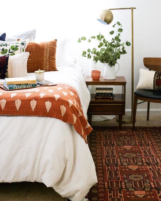 a fall colored bedroom with rust and orange textiles, a burgundy rug and some chocolate brown here and there