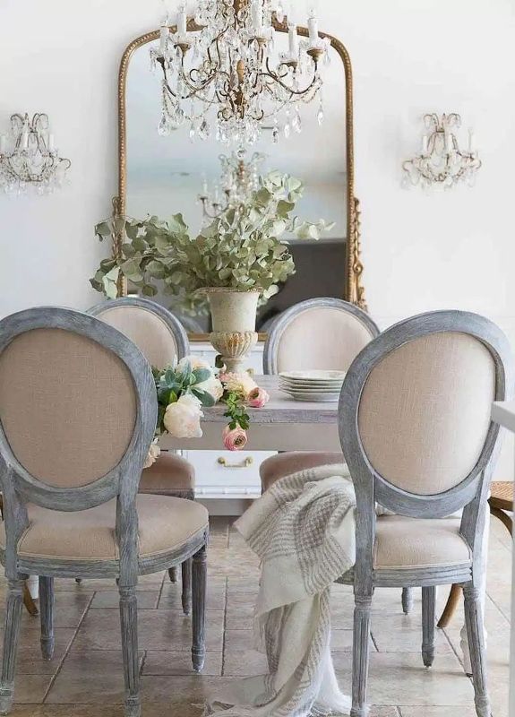 a fantastic dining room with a French feel, an oversized mirror in a gilded frame, a whitewashed table and neutral vintage chairs, a chic chandelier