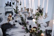a gorgeous Halloween tablescape with black, purple and white candles, greenery, roses, black porcelain, crows and skulls