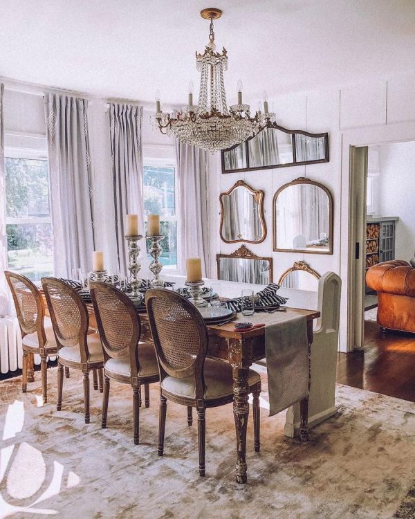 A jaw dropping French chic dining room with a stained vintage table, vintage chairs, a gallery wall of mirrors and a crystal chandelier