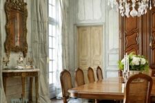 a jaw-dropping French chic dining room with paneling, a chic console table, a large stained table and chairs, a crystal chandelier