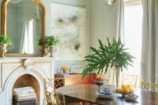 a lovely French chic dining room with light blue walls, a non-working fireplace, a stained table and vintage chairs, a large crystal chandelier