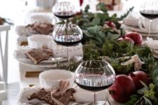 a lush winter tablescape with a greenery runner with pomegranates, gingerbread bcookies and elegant cutlery