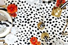 a modern glam Halloween tablescape with a Dolmatin runner, printed plates, brigth blooms, gold candleholders and black spiders