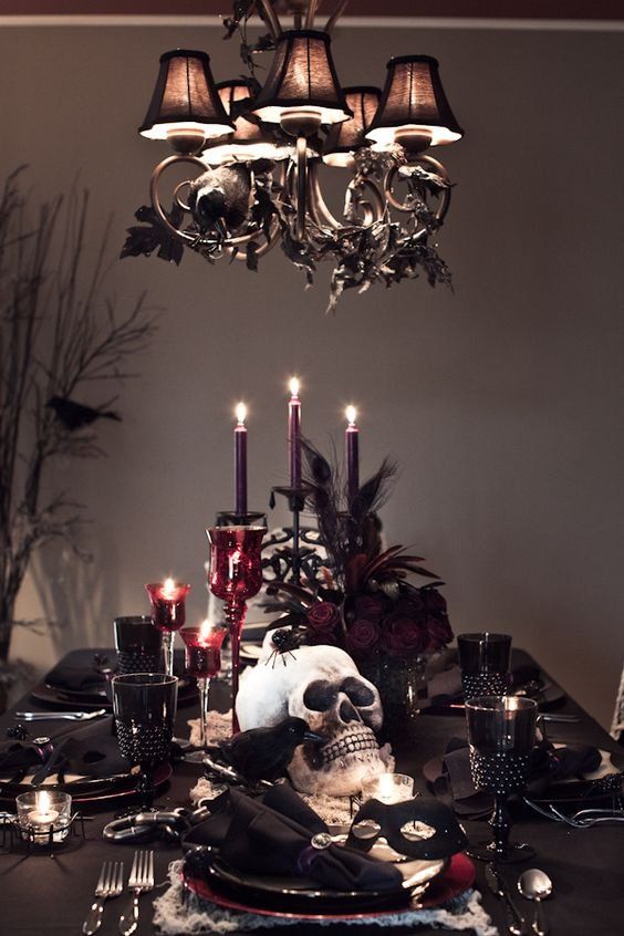 a moody and chic Halloween tablescape with black linens, purple candles and deep red blooms, skulls, crows, spiders and black goblets