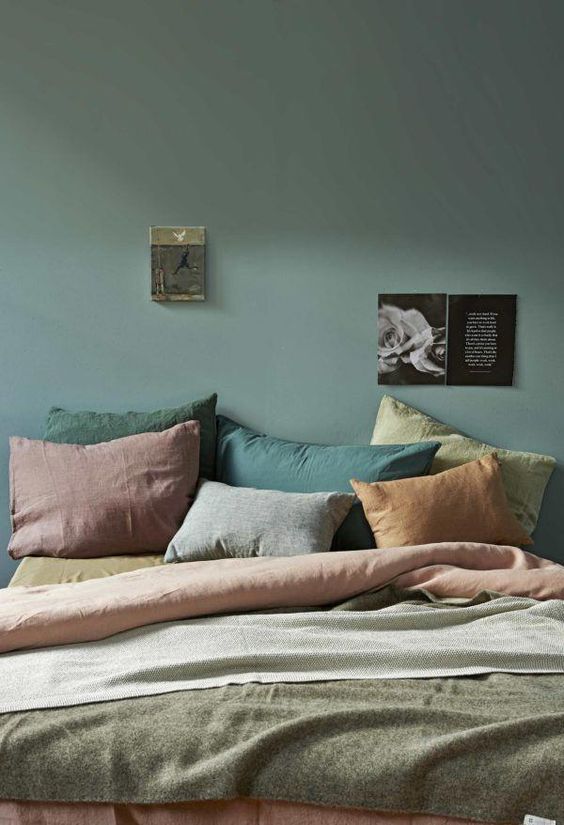 a muted-colored bedroom with a dark green wall, pillows of muted shades like rust, greens and mauve