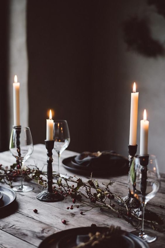 a natural Halloween table setting with candles, dried branches with berries, greenery and black plates